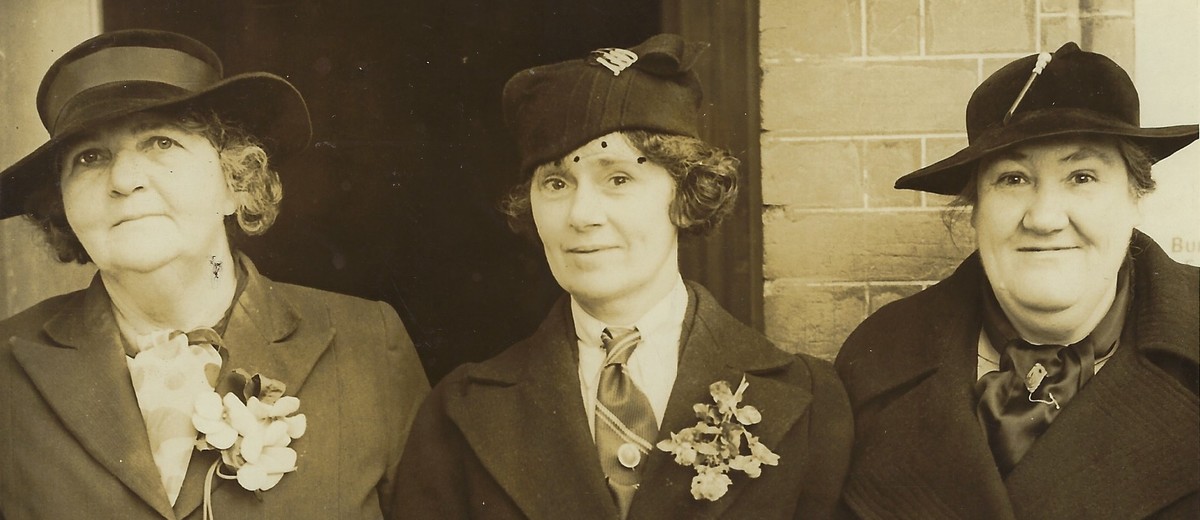 Three women standing together, all wearing hats and coats. 