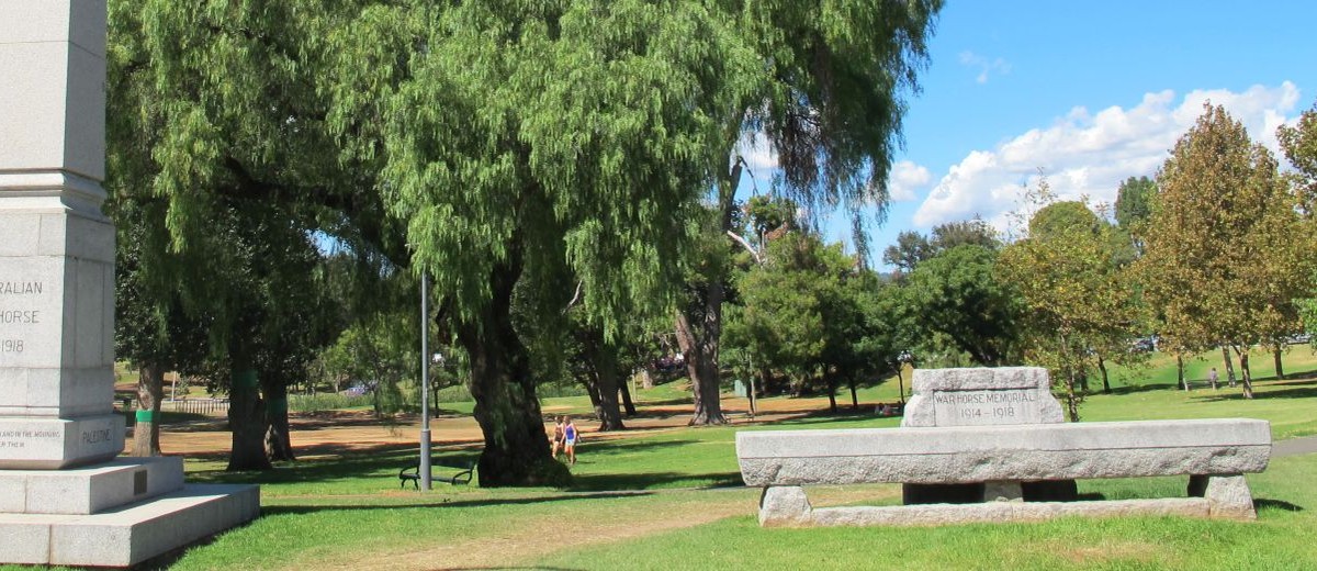 Image: a stone pillar and trough commemorating the Australian Light Horse and warhorses (1914-1918) are situated in a public park with a variety of trees and expanses of grass
