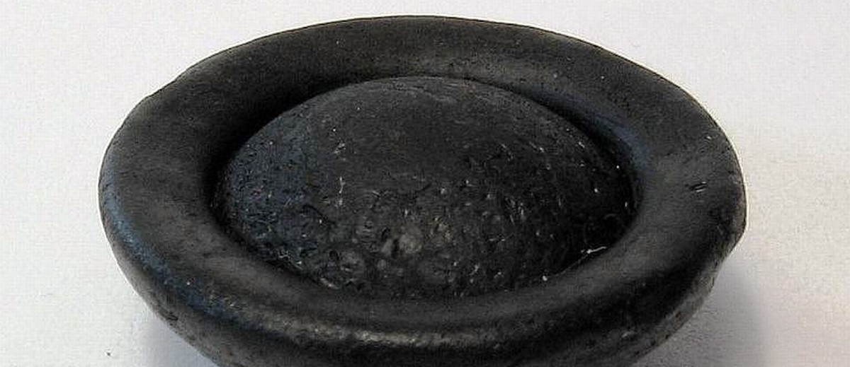Image: A black button-shaped object made of natural glass. It is roughly circular, and features a convex face. The opposite face comprises a shallow depression with a central convex surface emerging from it