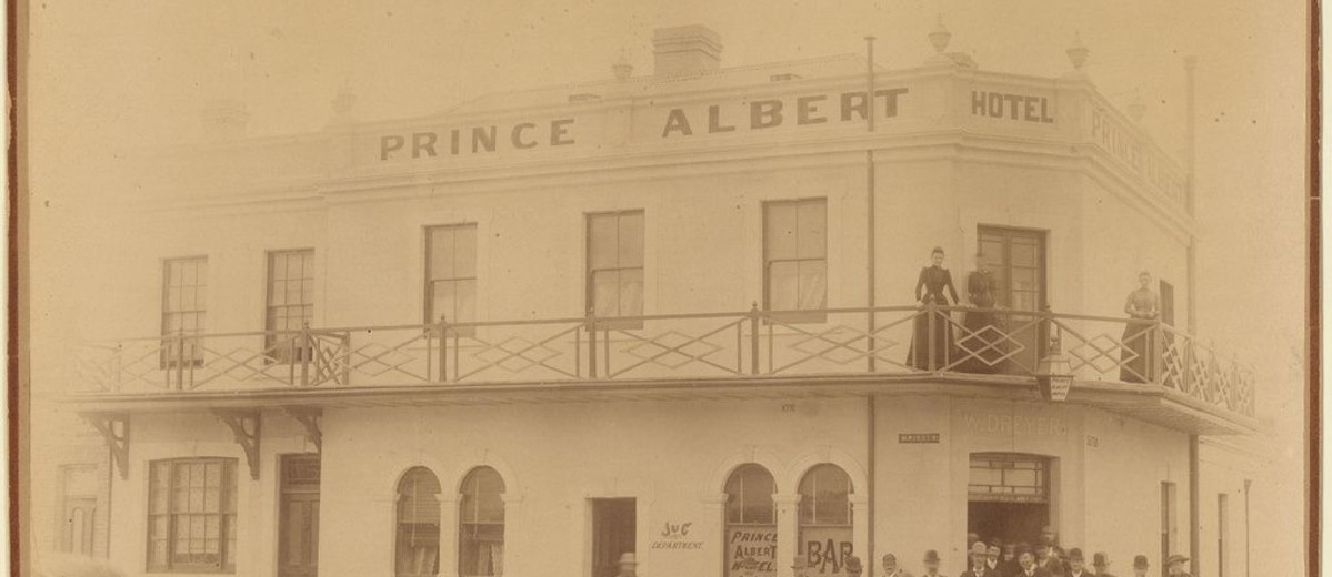 Image: group of people standing below and on balcony of large stone building