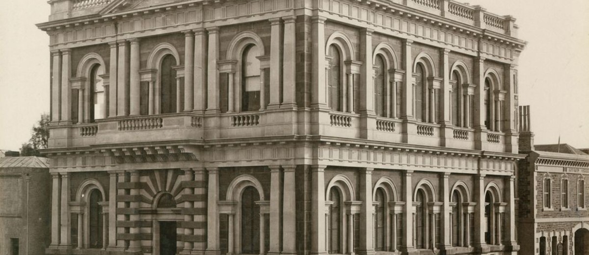 Image: Black and white photograph of a two storied stone building featuring arched windows
