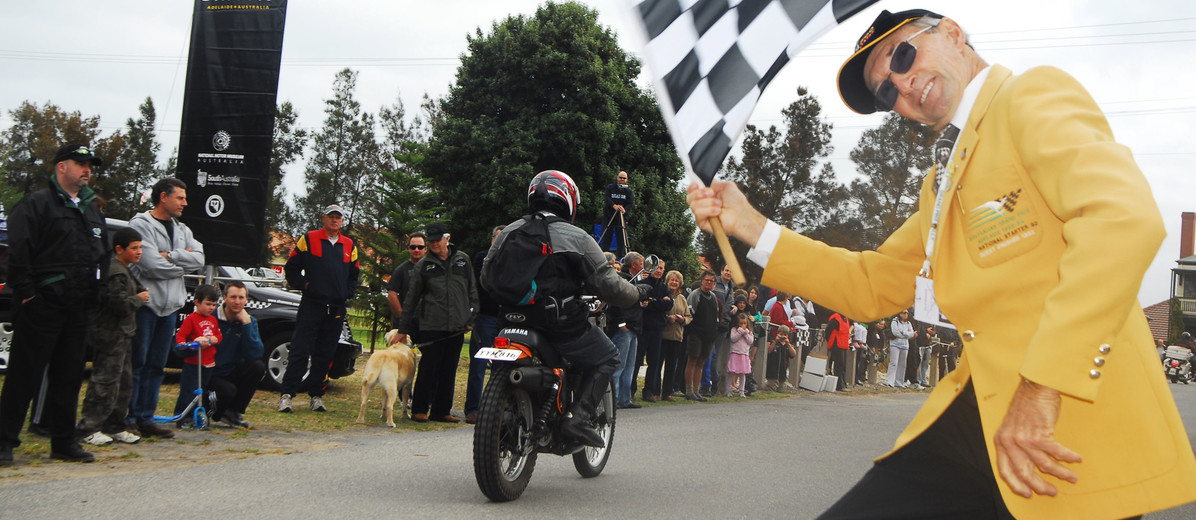 Image: man waving checkered flag as motorbike rides away