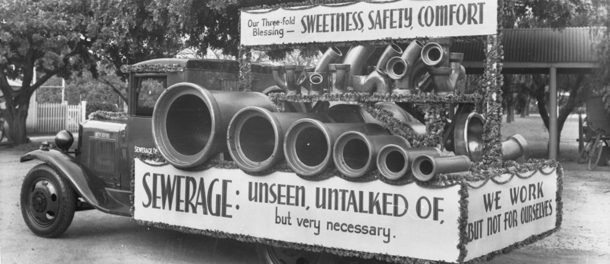 Image: truck carrying large pipes and sewer signage