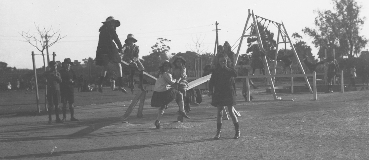 Image: A group of girls and boys play on playground equipment, including see-saws and swings