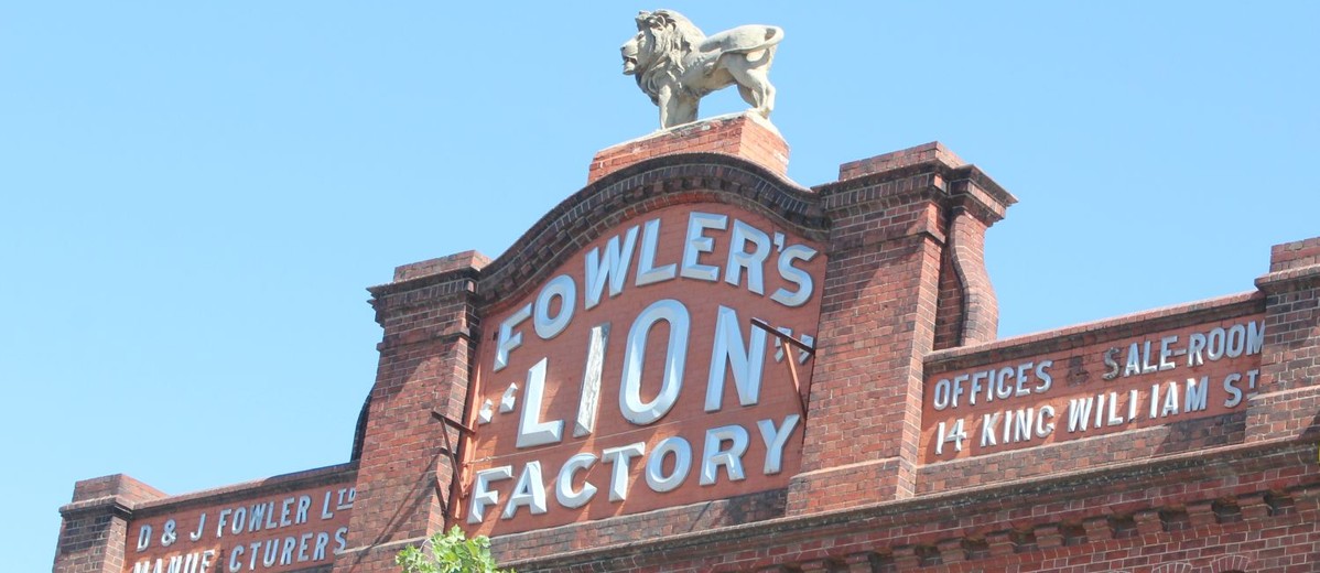 Image: Lion sculpture on top of red brick parapet baring signage 'Fowler's Lion Factory'