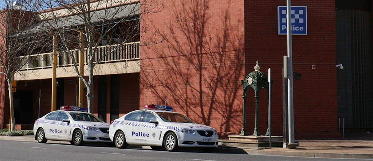 Image: Large red brick building on street corner with fountain and two police cars in front