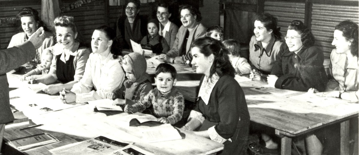 Image: man standing in front of group of women and children sitting at desks