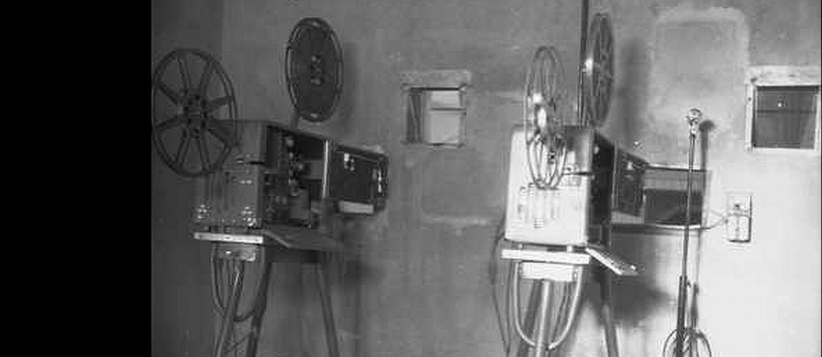 Image: Two film projectors of 1940s vintage stand in a projection room that is likely located within a cinema