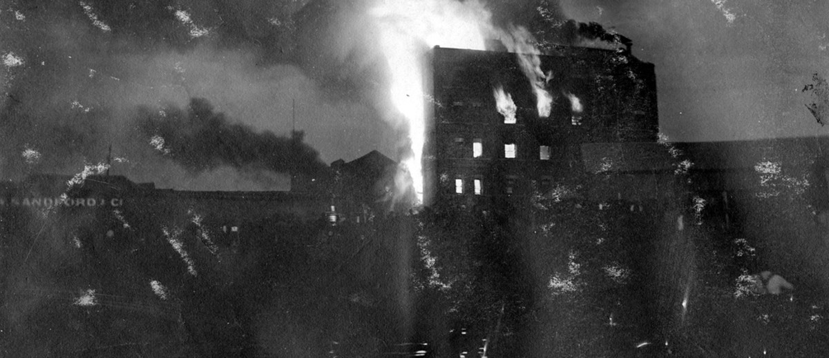 Image: A large, multi-storey building is completely consumed by fire. The blaze is taking place at night, and in close proximity to a river