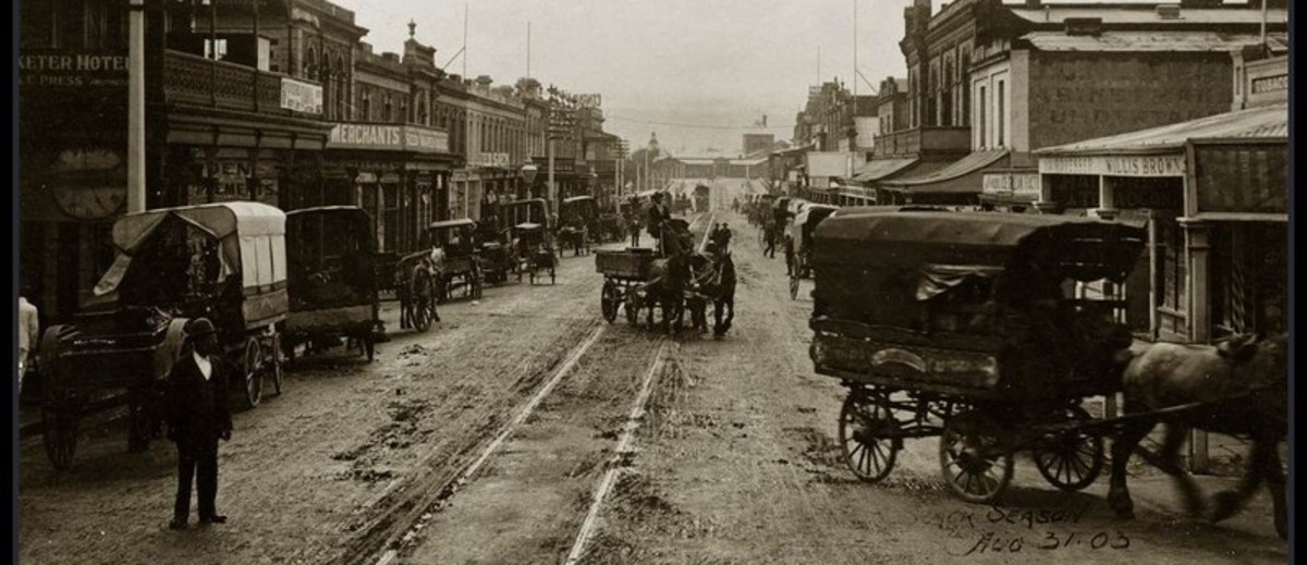Image: horse drawn carriages on dirt city street 