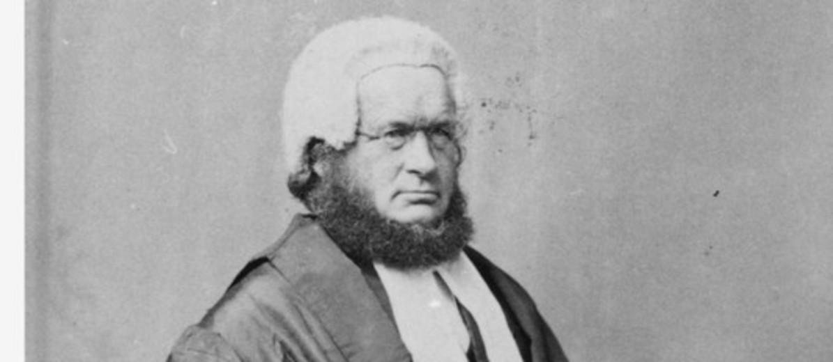 Image: Black and white portrait of a man, with the chin curtain beard popular at the time. He is seated and wearing his wig and gown.