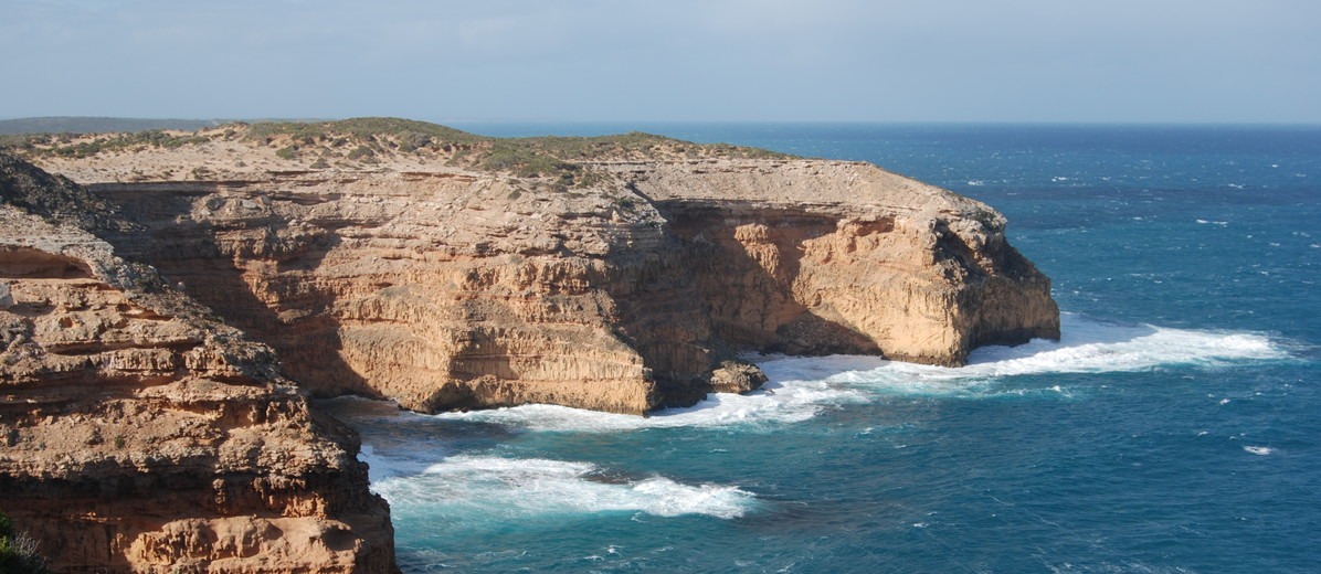 Image: A large bare cliff face juts out into the ocean