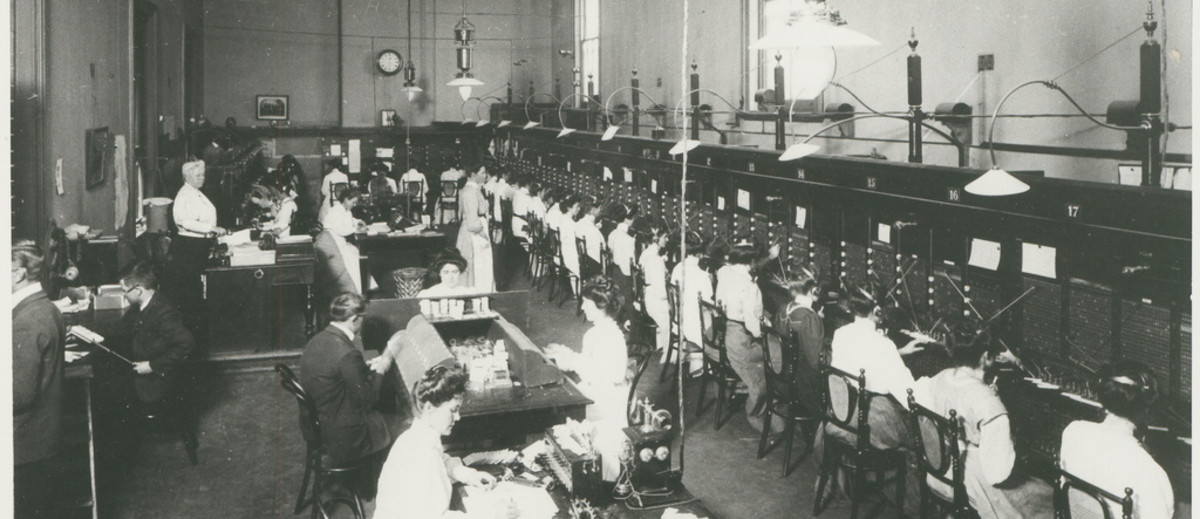 Image: A busy telephone exchange. There are rows of switchboard operators and several other staff supervising