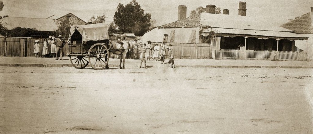 Image: horse and cart on dirt street with group of people, including young children, surrounding