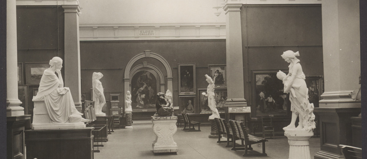 Image: The interior of an art gallery with high ceilings. Six white statues and numerous portrait paintings are in view