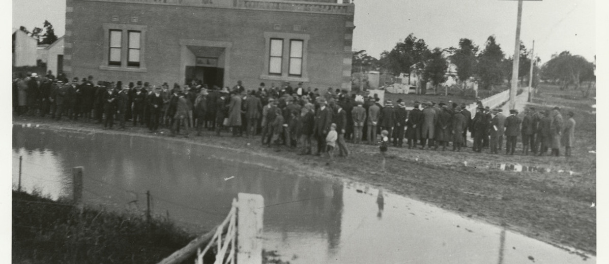 Image: A building with a large group of men gathered around the front. 