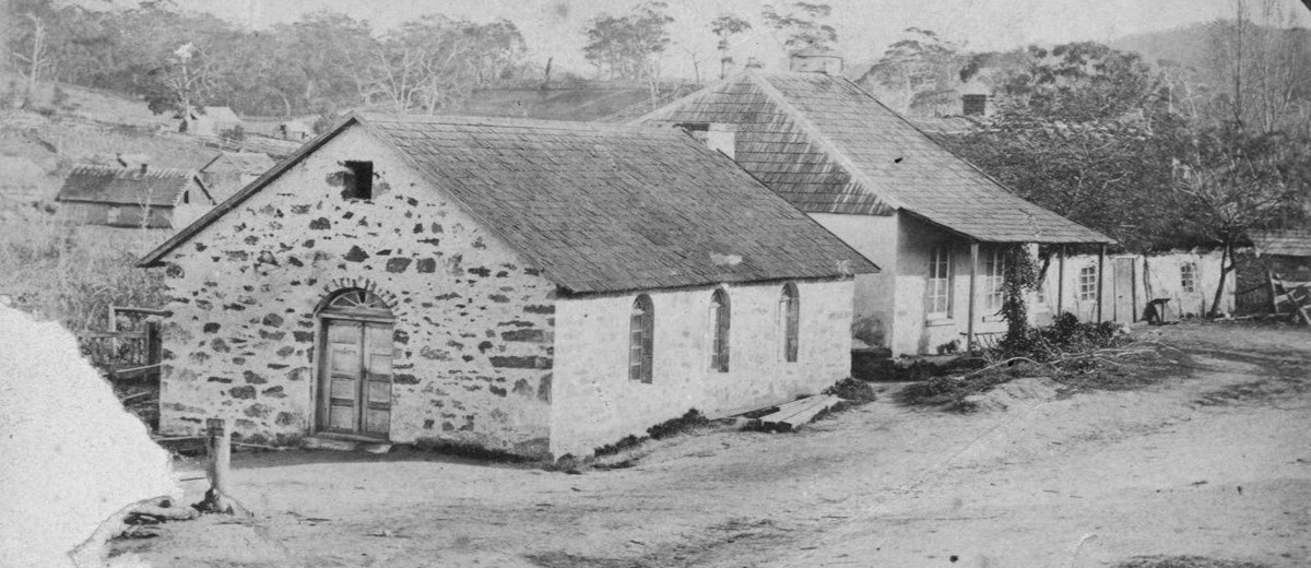 Image: Two gable roof, stone cottages sit adjacent to each other with the hills and gum trees of Lobethal in the background