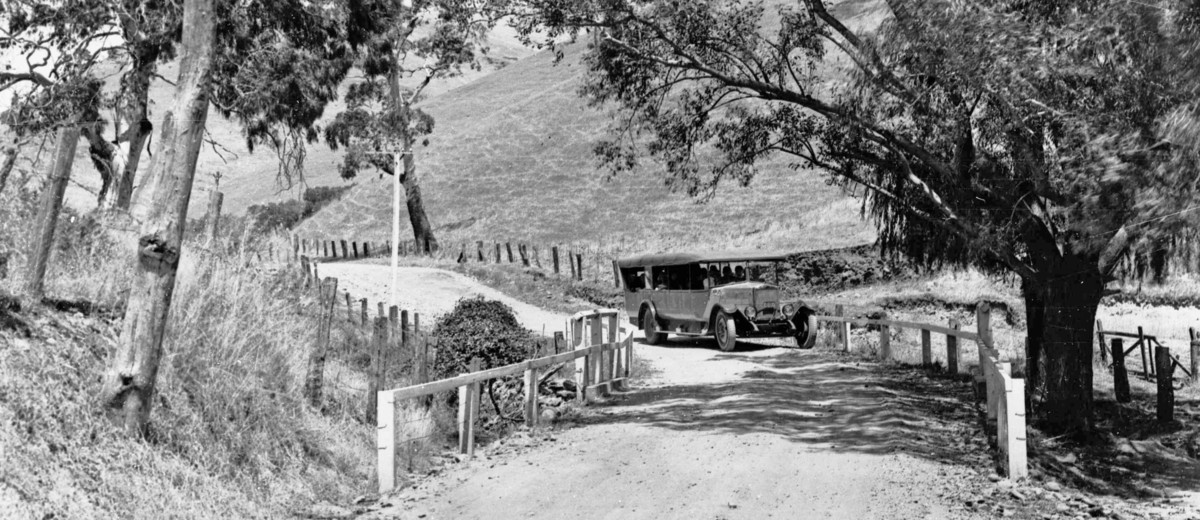 Image: A charabanc travelling along a road with fence post barriers to delineate the sharp corner for speeding motorists, 1920s.