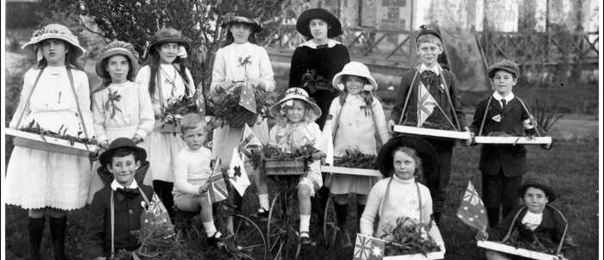 Image: A group of children stand near a house holding trays of flowers, two are on bicycles, and some are holding Australian flags