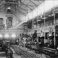 Image: a large open hall with a second storey gallery with flags hung from the railing. Rows of chairs and glass cabinets displaying various items fill the ground floor.
