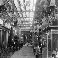 Image: A line of displays fill a large hall. In the foreground of the photograph a glass cabinet topped with a large wooden horse holds leather harnesses and other tack. 