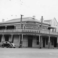 Image: a two storey corner hotel with balcony. A 1940s era car is parked outside. Signs on the upper level advertise West End Exhibition Stout and Seppelts wine.