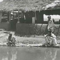 Image: Three men gather around a pool in front of a wooden framed building with a half mud-brick wall and thatched roof.