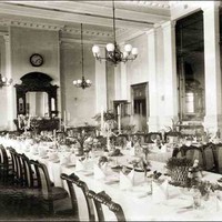 Image: a large dining room with multiple tables set with white cloths, candelabras and floral centrepieces.  