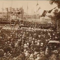 Image: a huge group of people in 1880s dress and hats surround a stage where a foundation stone is being laid.