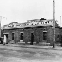Image: a single storey brick building with a low pitched roof behind a parapet sign reading "Balfour, Bricknell & Co. Ltd. Cake Specialists". To the right is a corrugated iron building with part of a sign visible reading "South Aust"