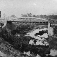 Image: a bridge with an arched parapet spans a small river in a deep valley