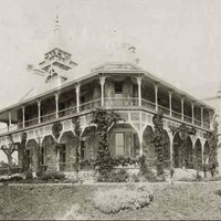 Image: Black and white photograph of two-storey stone house with wrap-around verandas on both levels