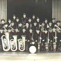 Image: A large, all-male brass band poses with their instruments on a stage