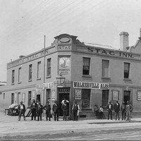 Image: A group of men stand outside a two storey corner hotel. Signs name it the Stag Inn and advertise Walkerville Ales for sale.