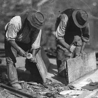 Image: Two men in hats are bent over splitting slate