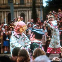 Image: a number of clowns parade past a crowd with a large number of children as part of a Christmas pageant