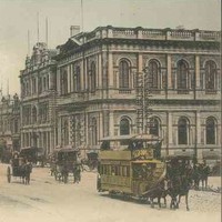 Image: horse drawn buses and carts travel down a busy city street lined with large commercial buildings