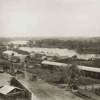 Image: a collection of stable buildings on the bank of a river.
