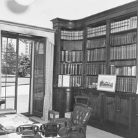 Image: A room containing shelves full of books and a wooden desk with chair