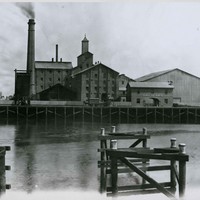 Image: View across river of large brick buildings and chimney with smoke