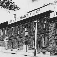 Image: A large complex of stone two-storey buildings next to a street. A sign on the front of the building reads ‘James Martin & Co., Iron Founders’