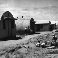 Image: children playing in dirt ditch in front of row of curved tin buildings