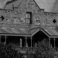 Image: A large, three-storey mid-nineteenth century bluestone building fronted by a dirt street. A sign reading ‘Prince Alfred Sailors’ Home, 1871’ is visible above the front entrance