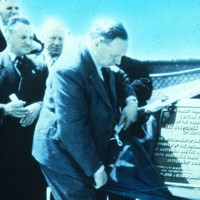 Image: A middle-aged man in a suit unveils a monument draped in an Australian flag while other similarly-clothed and aged men look on
