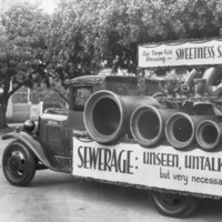 Image: truck carrying large pipes and sewer signage