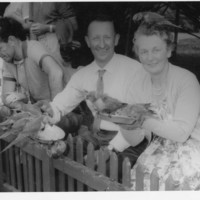 Image: a man and woman looking at camera while feeding pigeons
