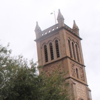 Image: A sign for Holy Trinity Church stands in front of the large stone church tower