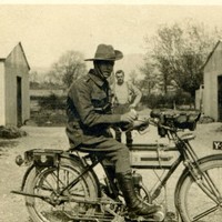 Sepia photo of a man in military uniform on a motorcycle. 