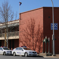 Image: Large red brick building on street corner with fountain and two police cars in front