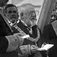 Image: A bearded middle-aged Caucasian man in Masonic ceremonial vestments officiates at a ceremony to lay a building’s foundation stone